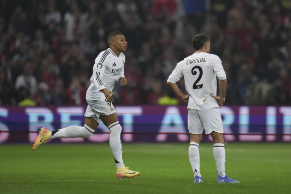 dramatic photo of mbappe clutching his hamstring during recent match, with militao and carvajal in treatment room backdrop